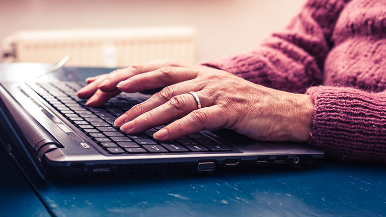 Senior women wearing wedding ring, typing on a laptop.